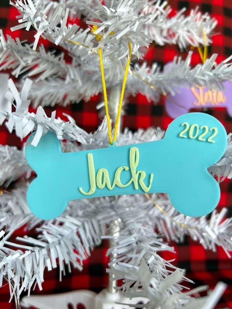 Blue personalized dog bone ornament reading Jack hanging on a white Christmas tree