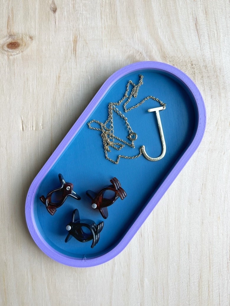 Blue on blue oval catch-all tray holding a necklace, a J initial charm, and earrings