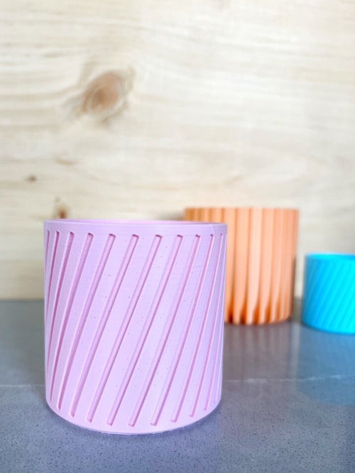 Empty pink diagonal stripe 3D printed planter with peach and blue pots in the background