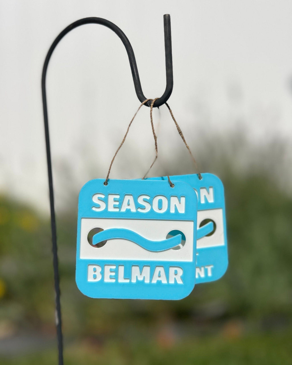 3D printed Jersey Shore beach badge ornament for Belmar in light blue, hanging outdoors from a garden hook