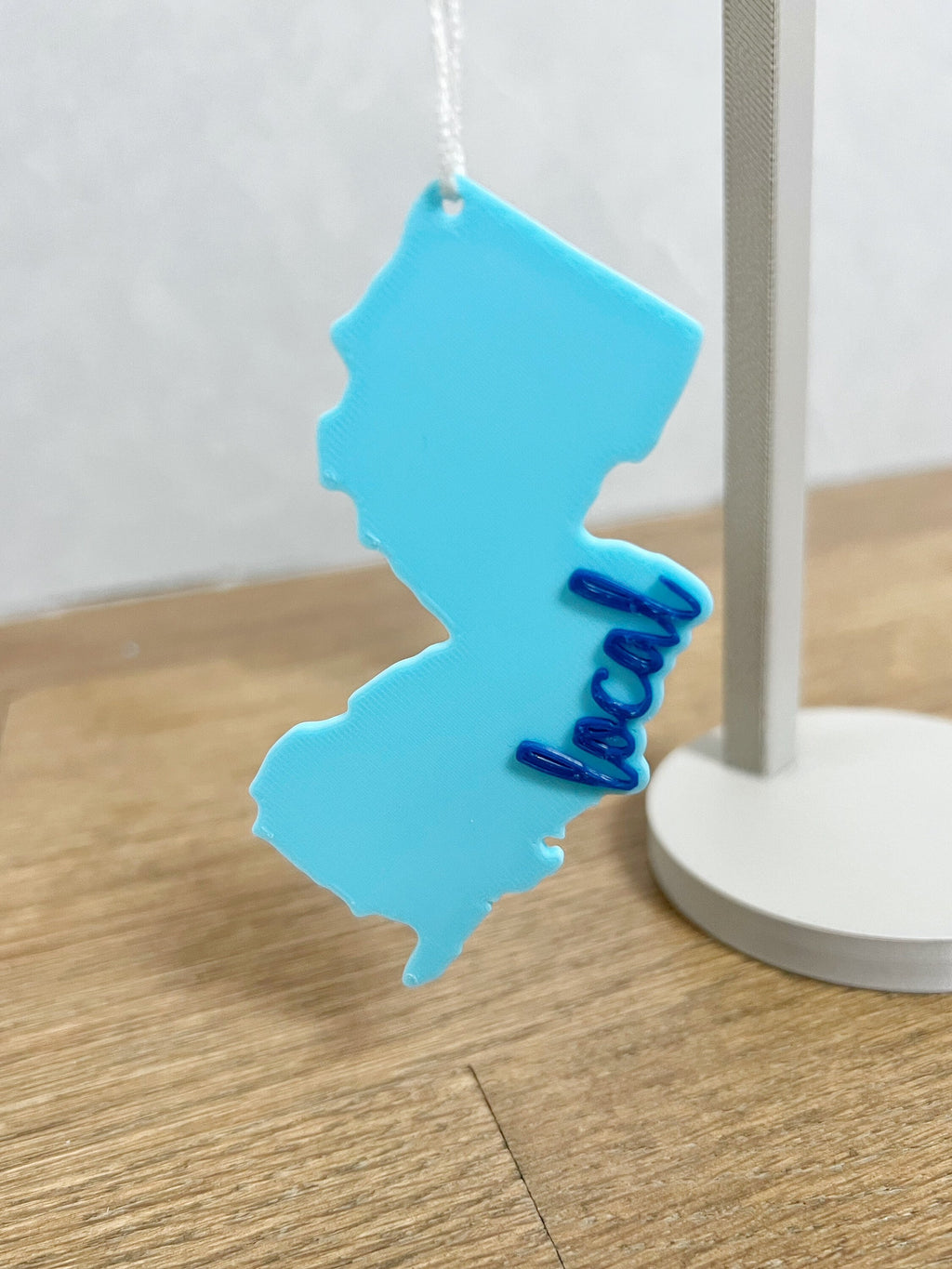 Light blue New Jersey local ornament hanging from an ornament stand on a wood floor