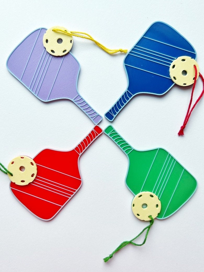 Four 3D printed pickleball paddle ornaments in purple, blue, red, and green with yellow balls