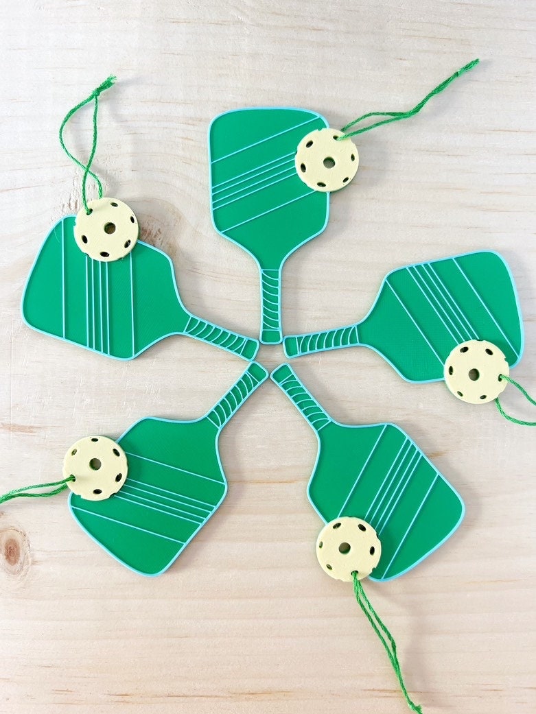 Five green pickleball paddle ornaments with yellow balls arranged in a circle on a wood surface