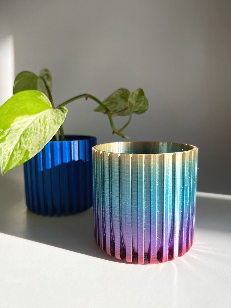 Rainbow gradient fluted 3D printed planter next to a blue one, with a pothos