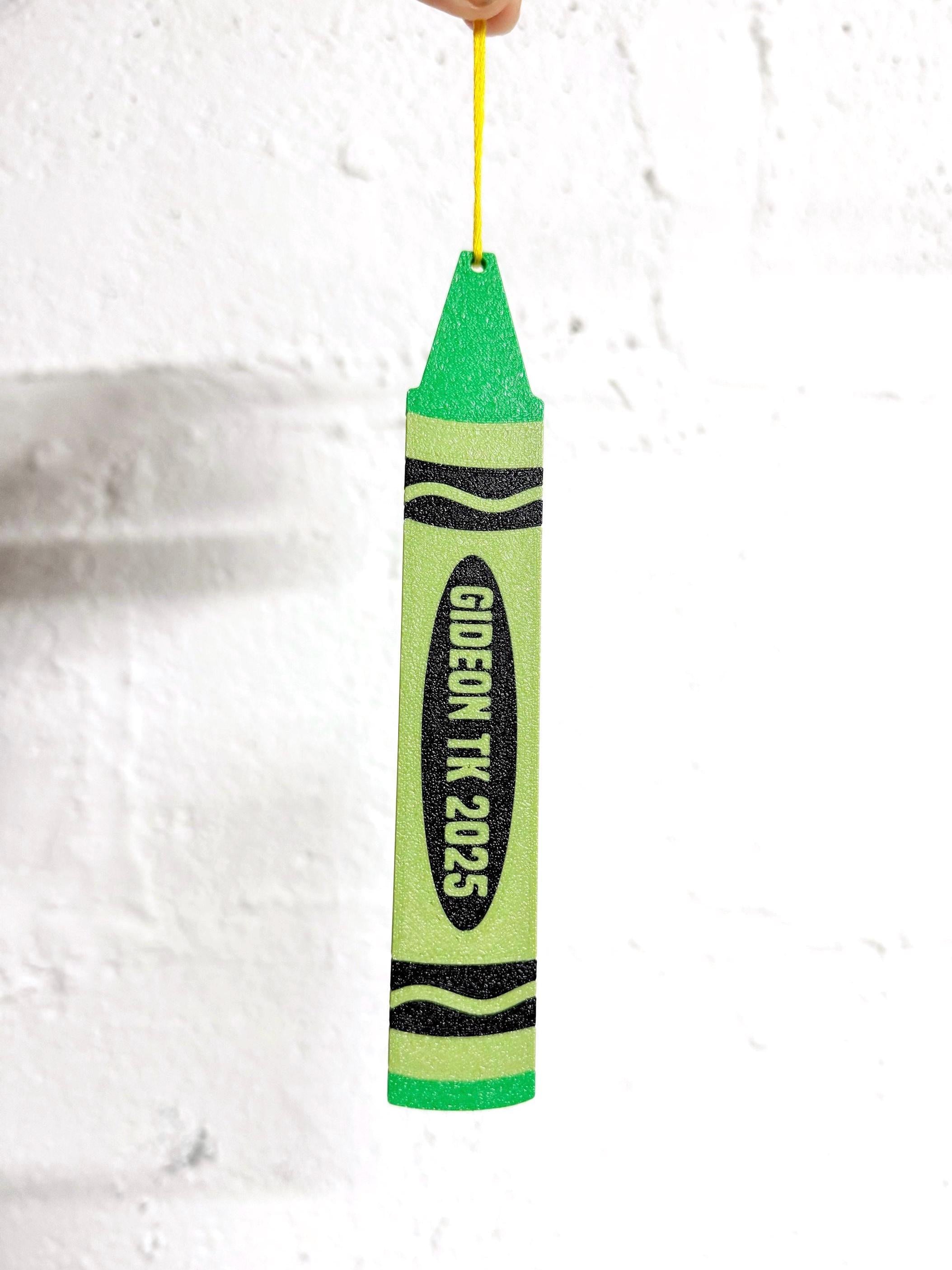 Green personalized crayon ornament reading Gideon TK 2025 hanging from a yellow string