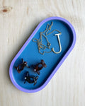 Blue on blue two-tone oval catch-all tray holding a gold necklace and earrings on a wood surface
