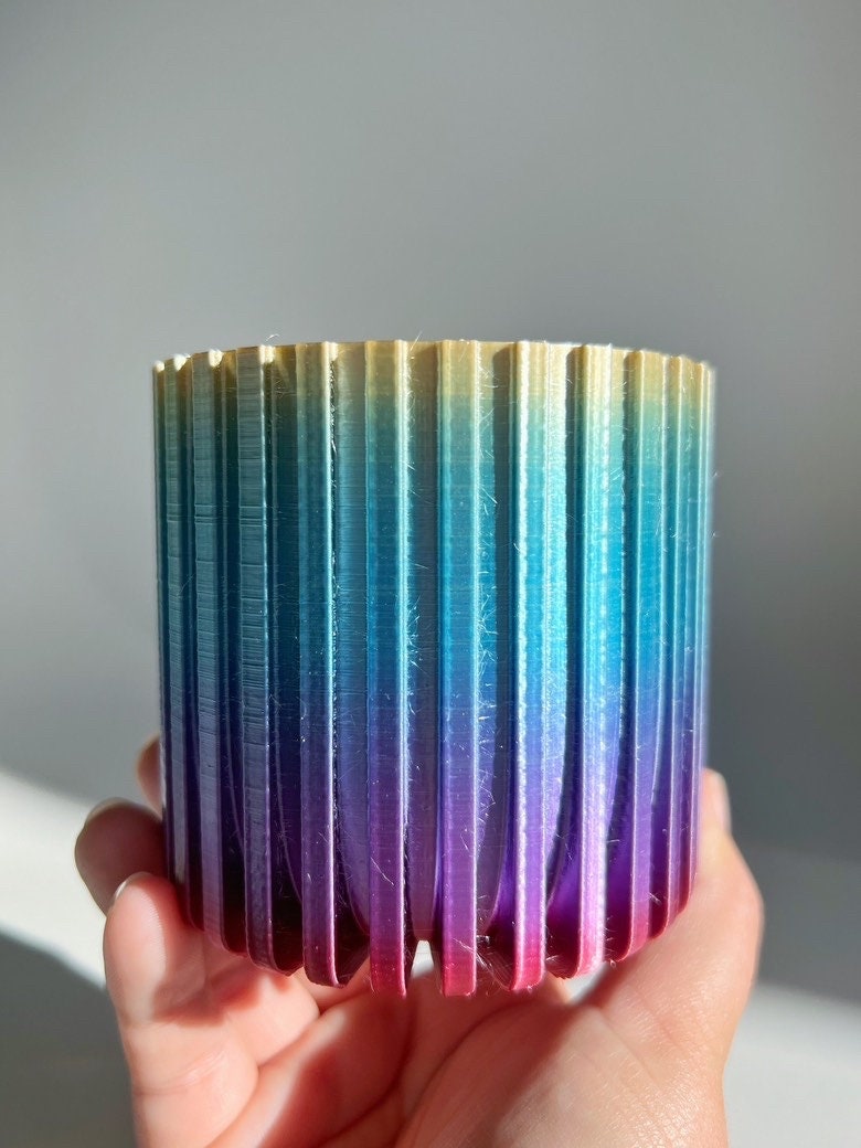 Hand holding a rainbow gradient fluted 3D printed planter, gold to blue to purple