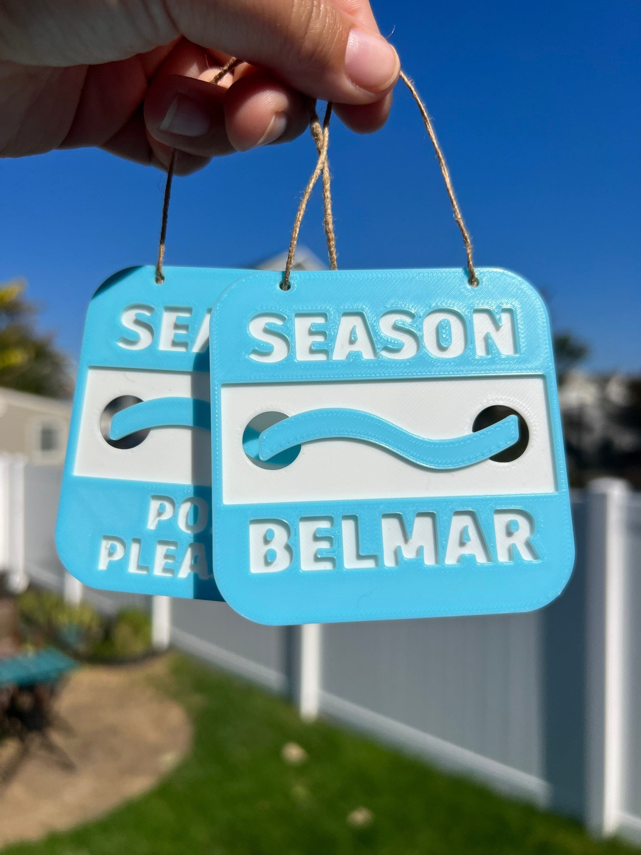 Belmar and Point Pleasant 3D printed beach badge ornaments held up against a blue sky
