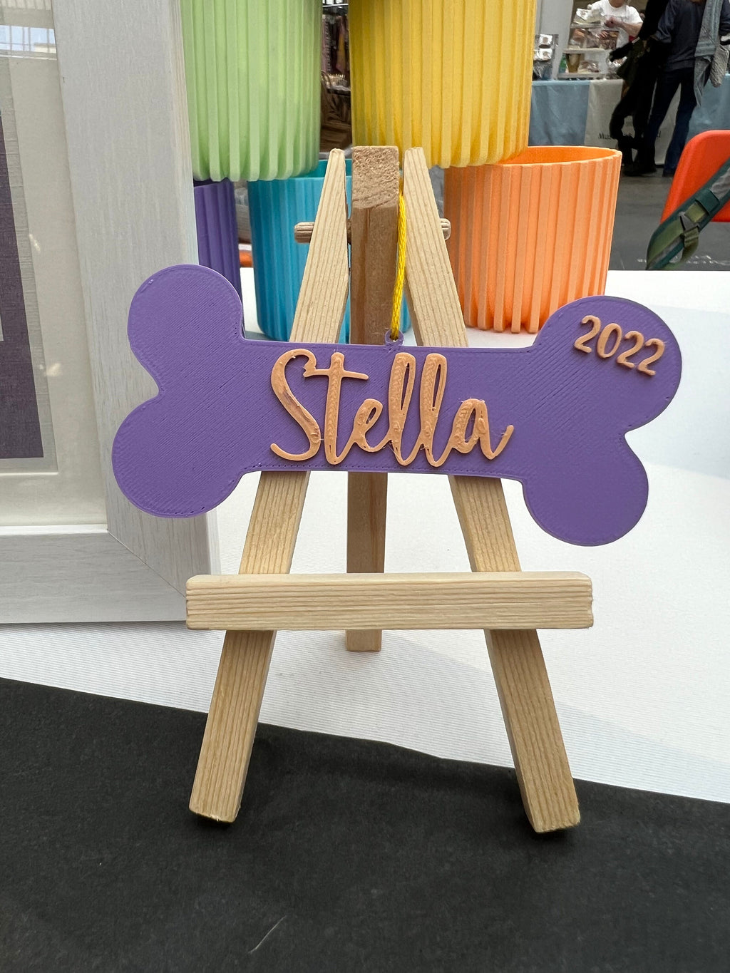 Purple personalized dog bone ornament reading Stella displayed on a small wooden easel