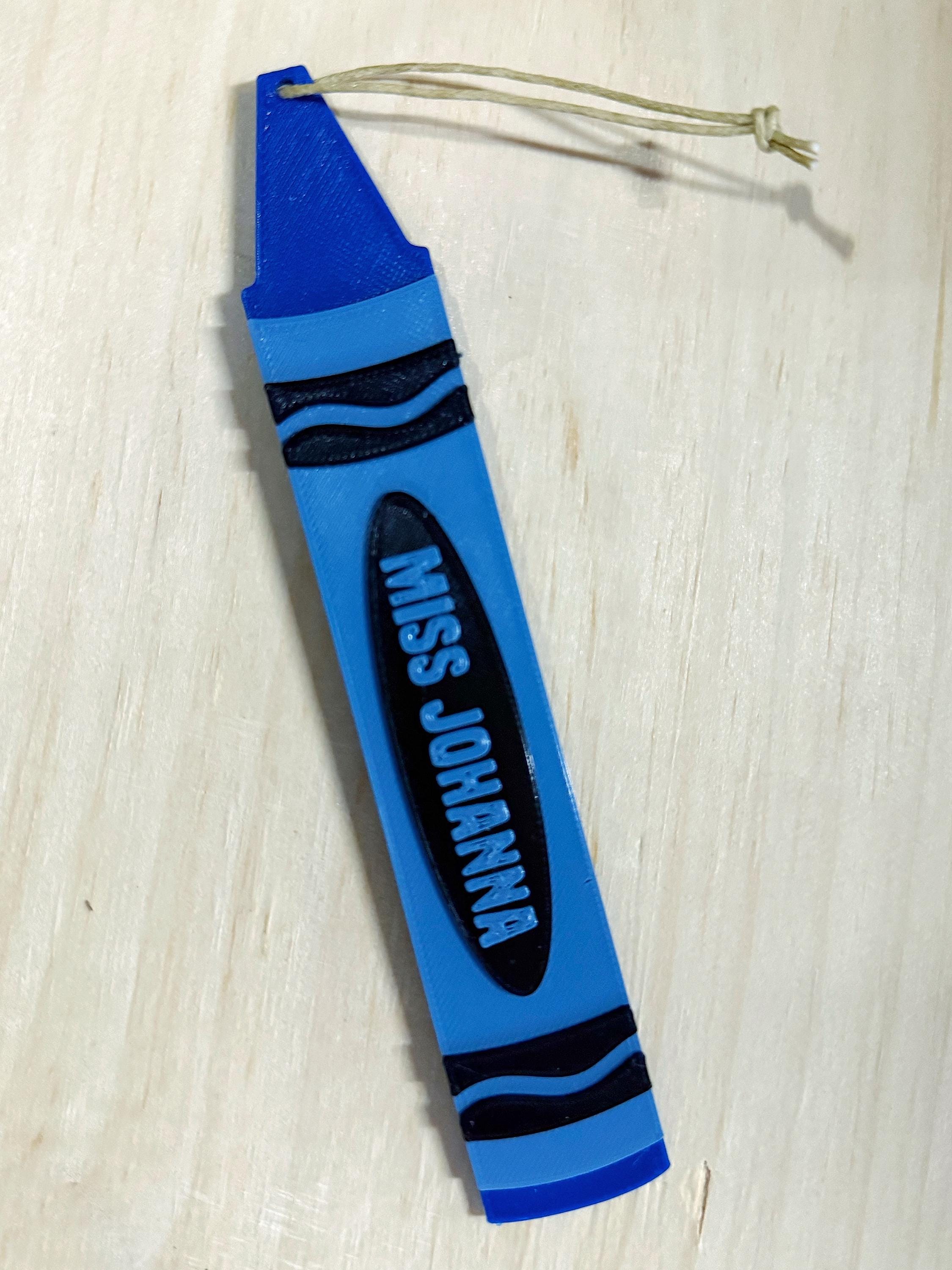 Blue 3D printed crayon ornament reading Miss Johanna with a twine loop on a wood surface
