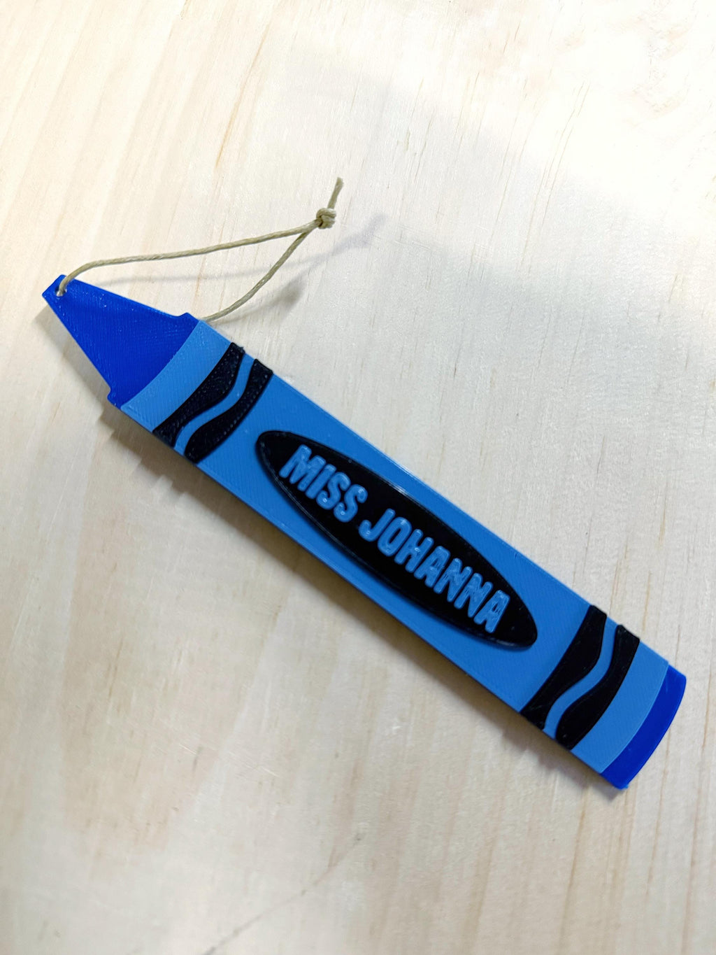 Blue personalized crayon ornament reading Miss Johanna laid at an angle on a wood surface