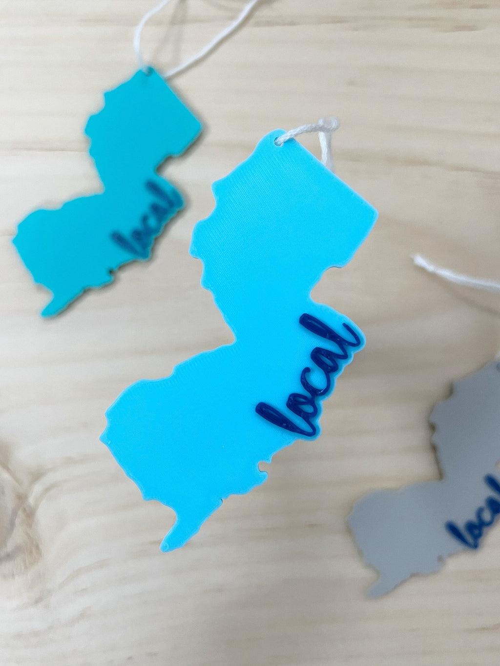 Three 3D printed New Jersey local ornaments in teal, blue, and gray on a wood surface