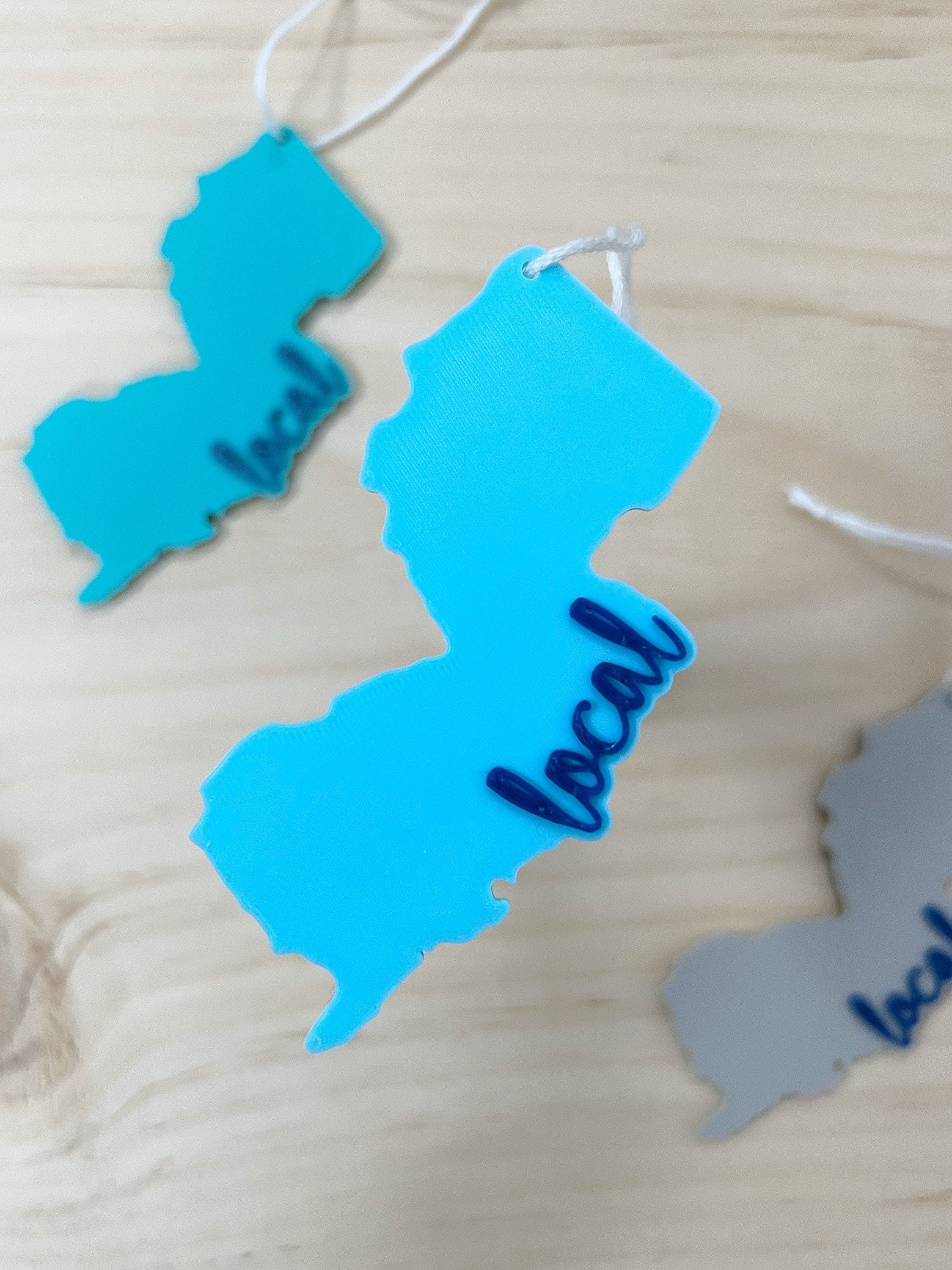 Three 3D printed New Jersey local ornaments in teal, blue, and gray on a wood surface