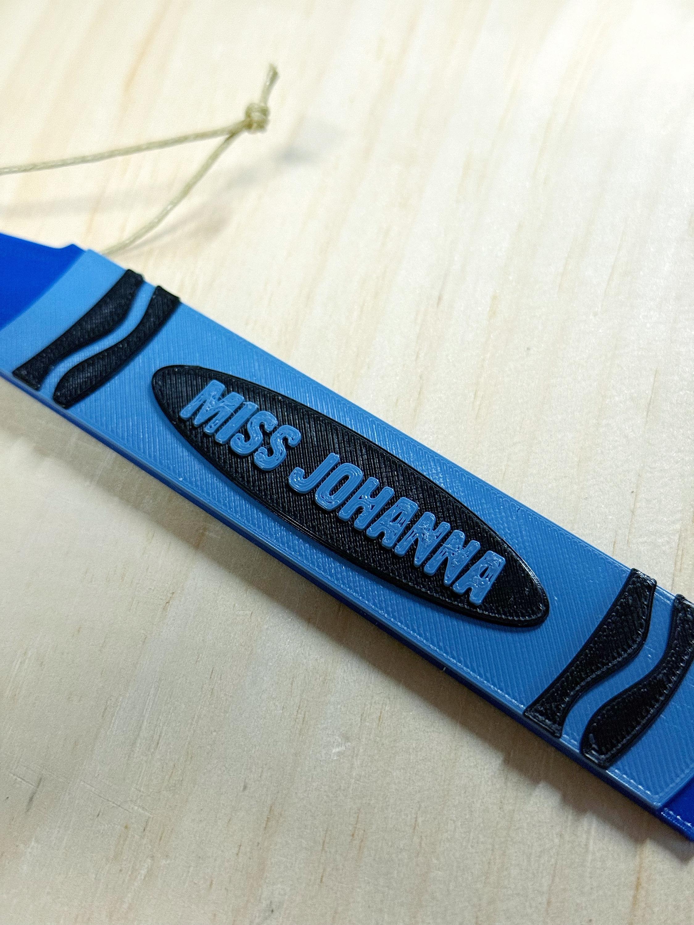 Close-up of a blue 3D printed crayon ornament with the name Miss Johanna in the center label