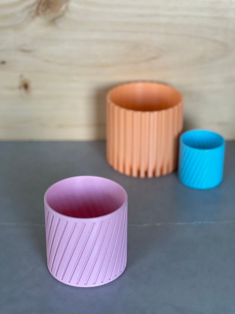 Pink diagonal stripe planter in front, with peach and blue planters behind
