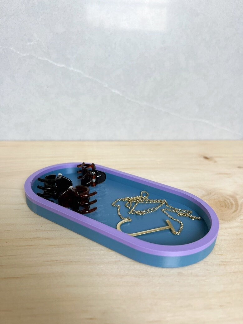Blue on blue oval catch-all tray holding a hair clip and gold jewelry