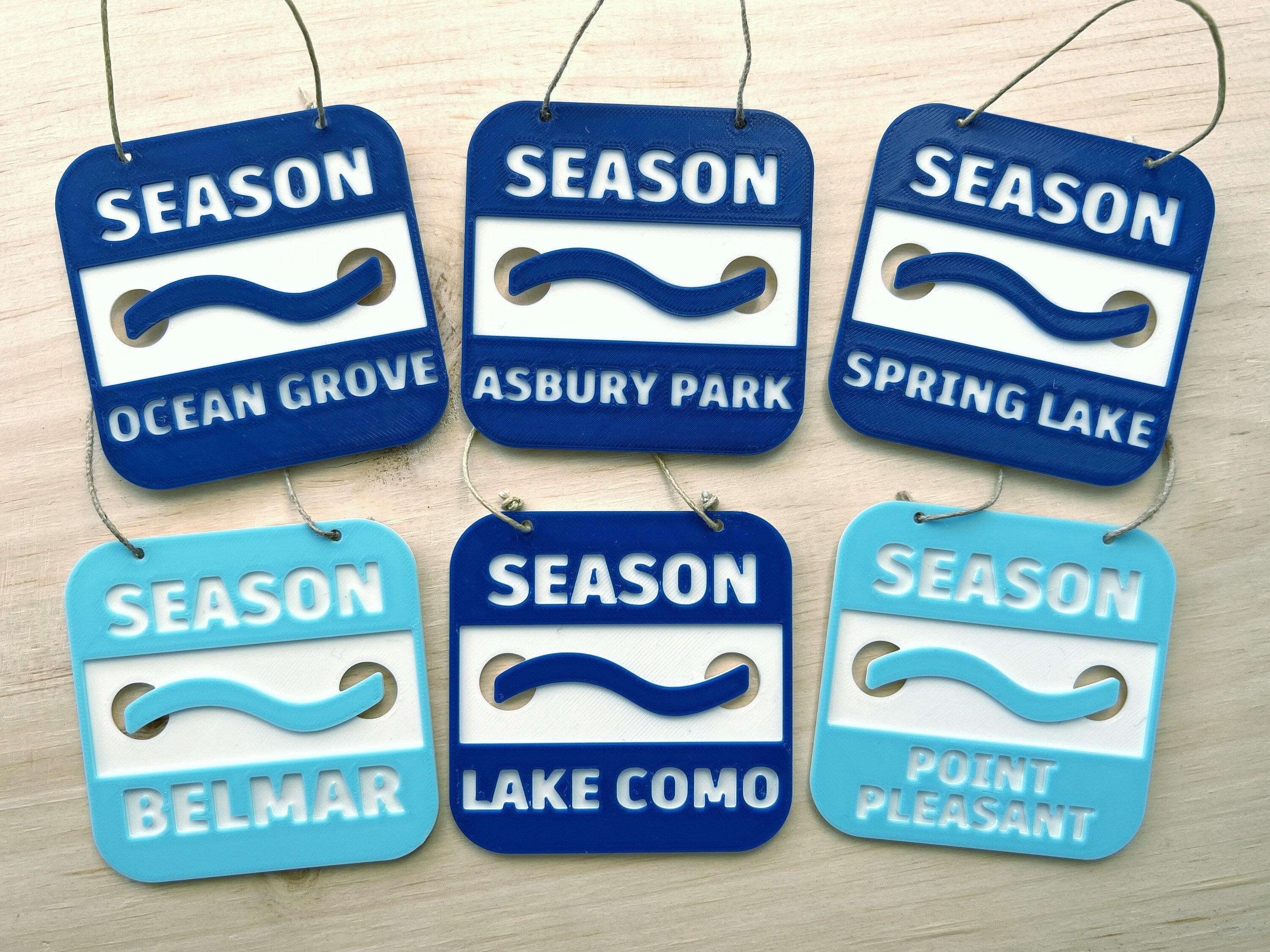 Six 3D printed Jersey Shore beach badge ornaments: Ocean Grove, Asbury Park, Spring Lake, Belmar, Lake Como, and Point Pleasant, in navy and light blue
