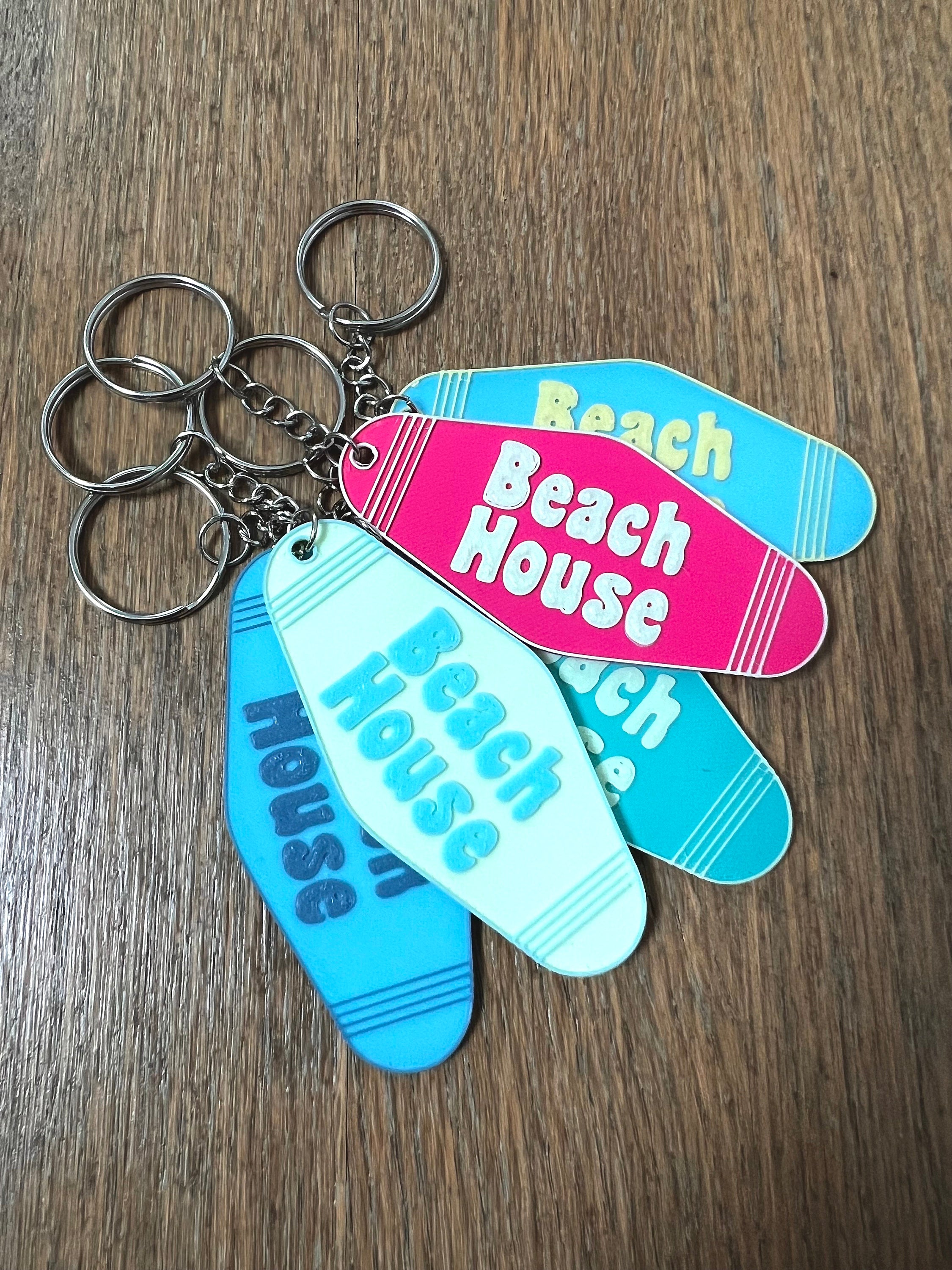 Stack of 3D printed Beach House keychains in pink, blue, and teal with key rings