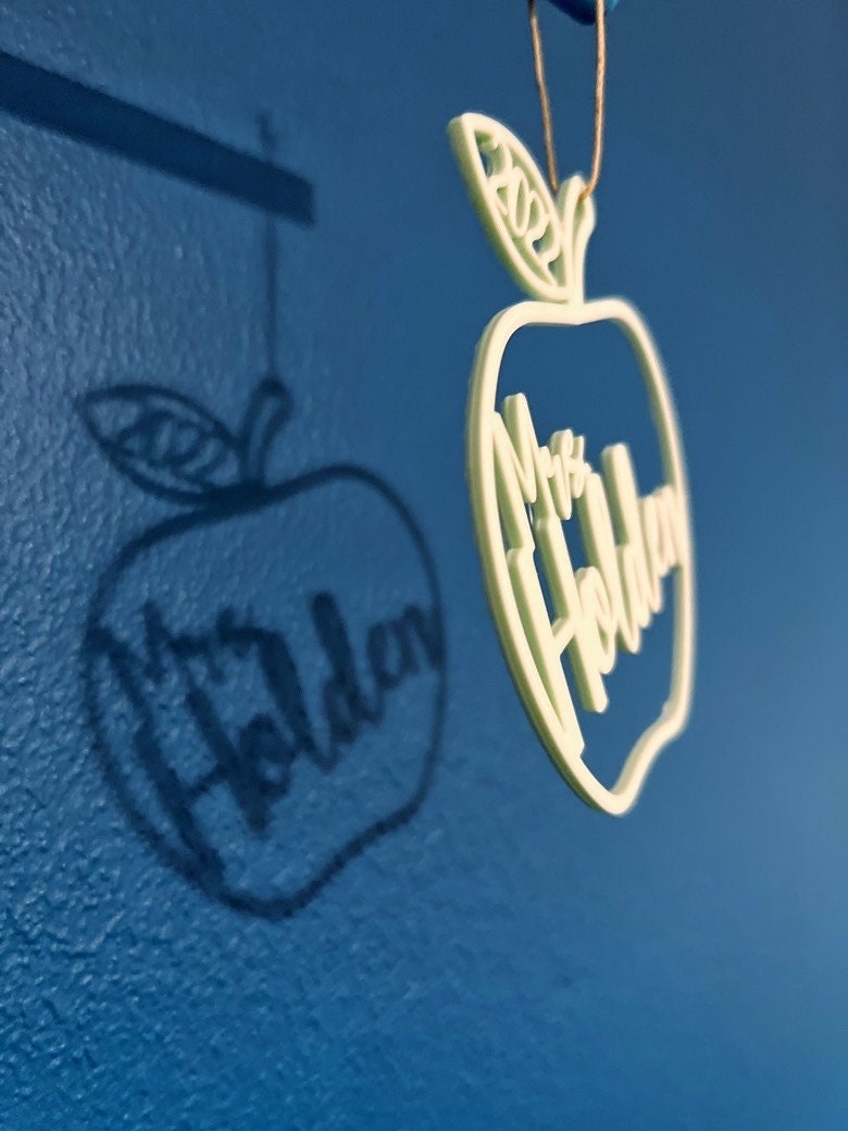Mint green apple ornament reading Mrs Holden hanging and casting a shadow on a blue wall