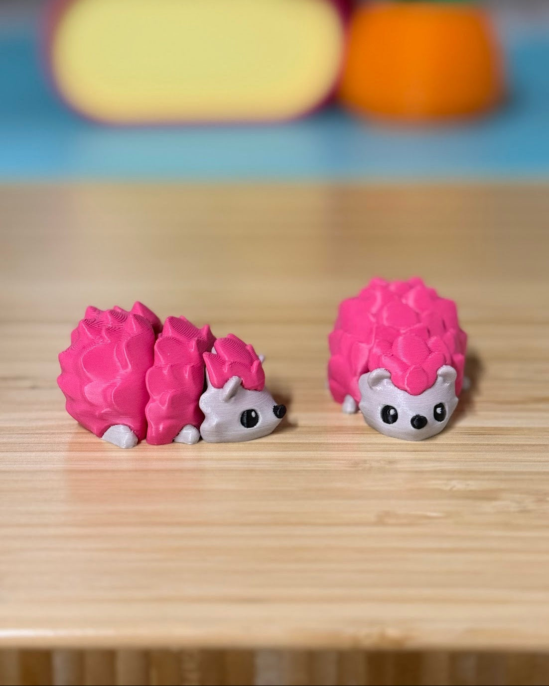 Two pink 3D printed Mini Flexi Hedgehog fidget toys on a wood desk