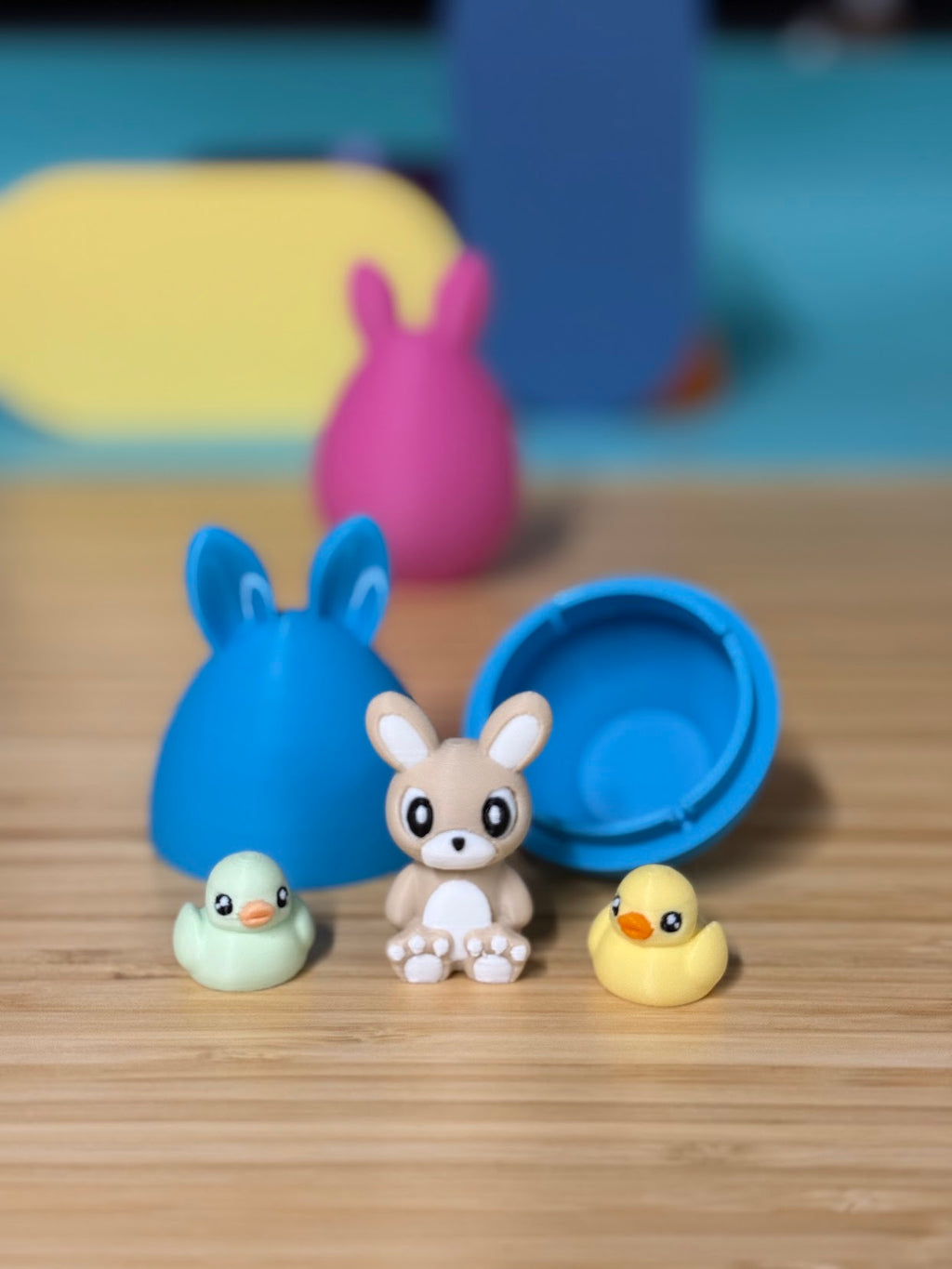 Blue 3D printed bunny ear mystery egg opened next to a small bunny, chick, and duck toy