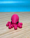 Pink 3D printed Mini Flexi Octopus fidget toy on a wood desk