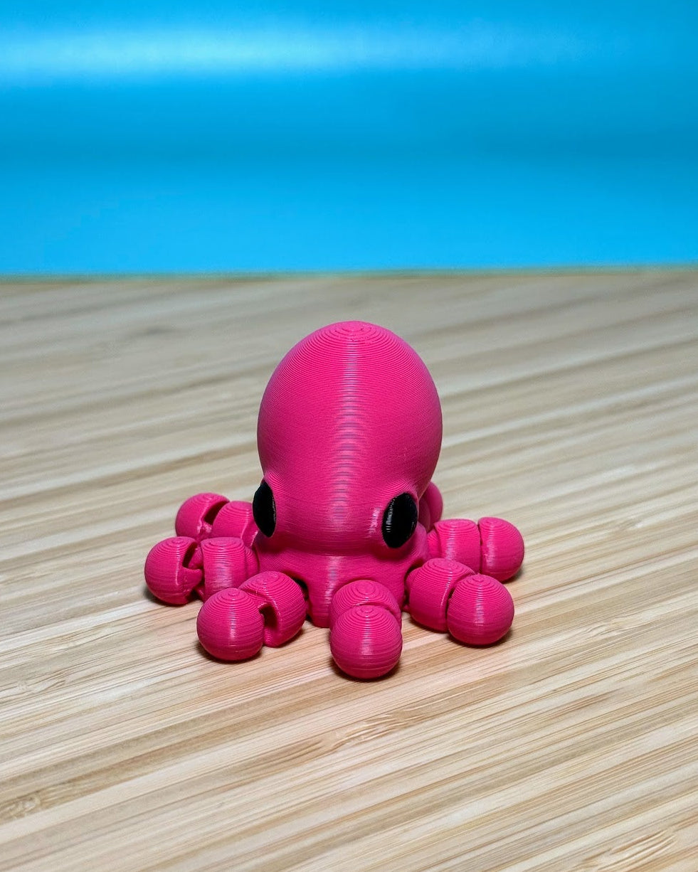 Pink 3D printed Mini Flexi Octopus fidget toy on a wood desk