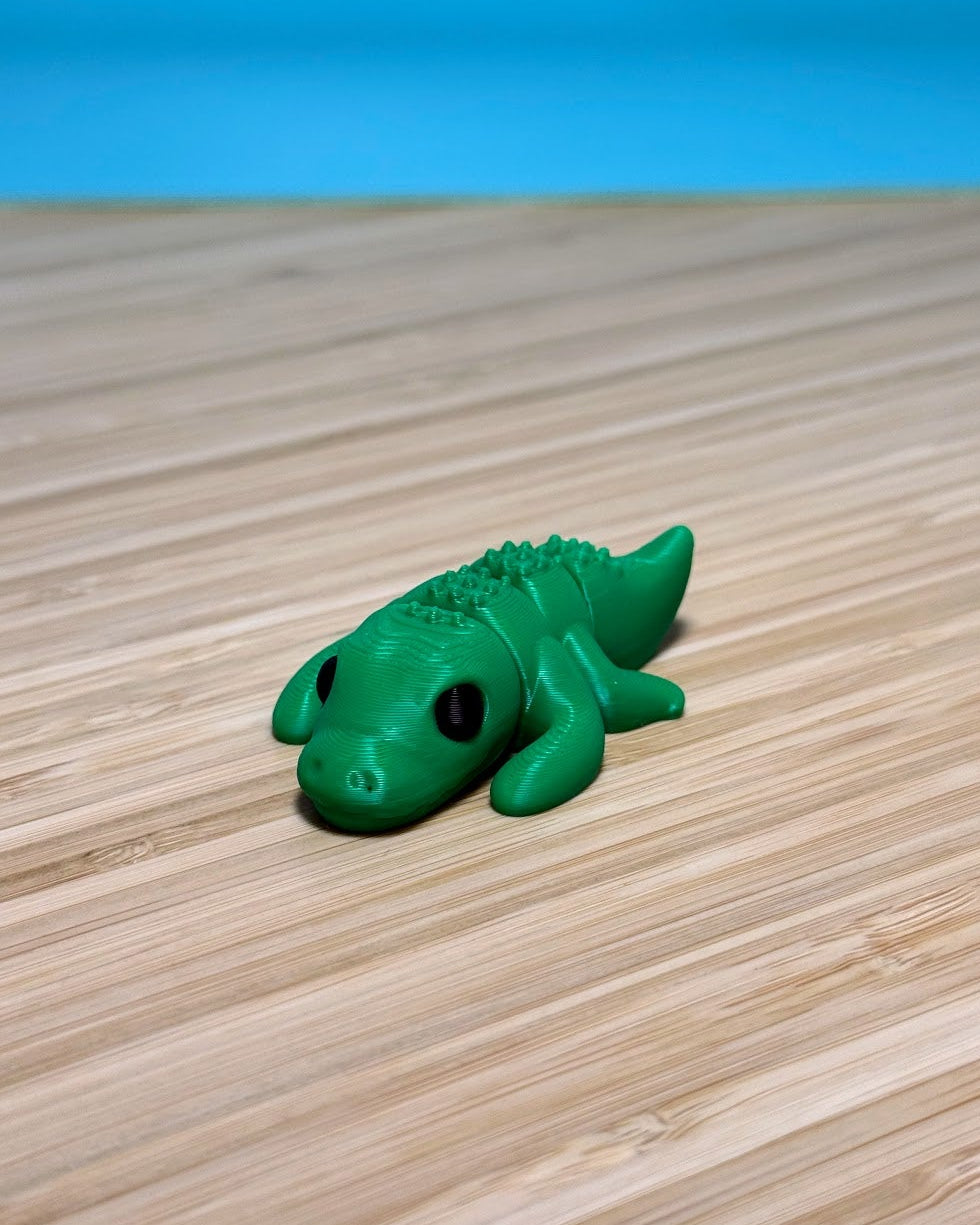 Green 3D printed Mini Flexi Alligator fidget toy on a wood desk