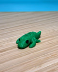 Green 3D printed Mini Flexi Alligator fidget toy on a wood desk