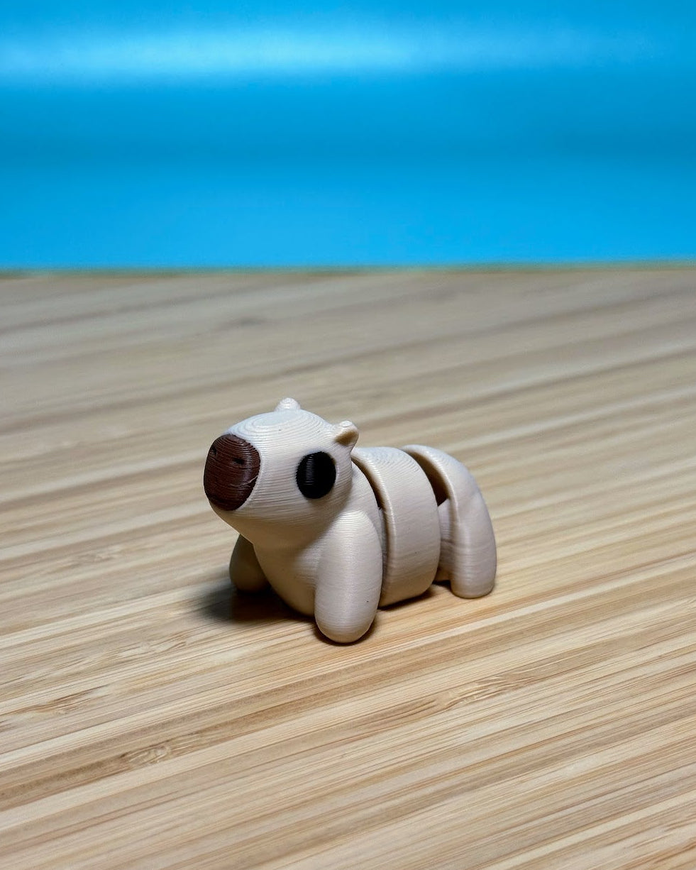 Tan 3D printed Mini Flexi Capybara fidget toy on a wood desk
