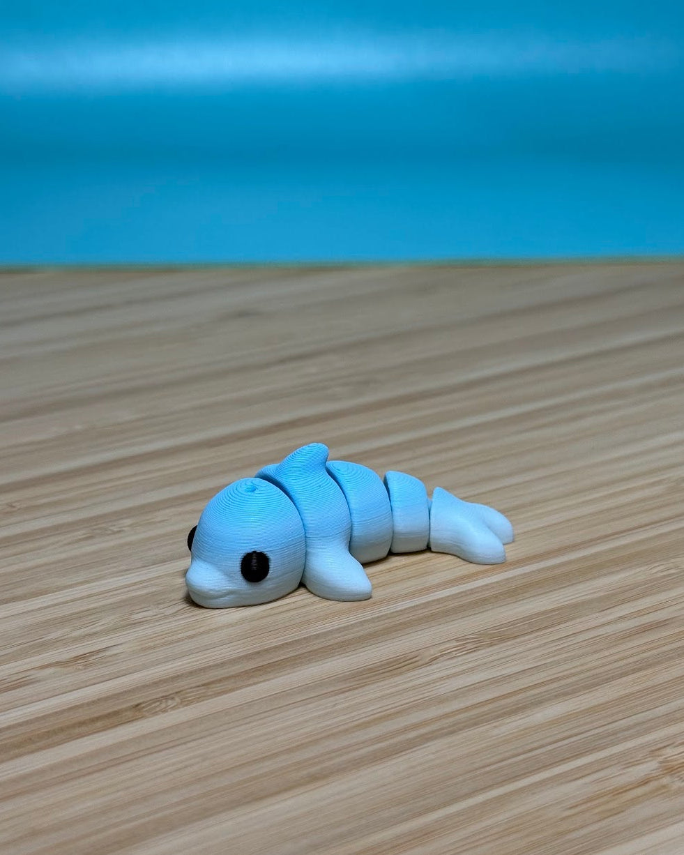 Light blue 3D printed Mini Flexi Dolphin fidget toy on a wood desk