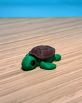 Green 3D printed Mini Flexi Turtle fidget toy with a brown shell on a wood desk