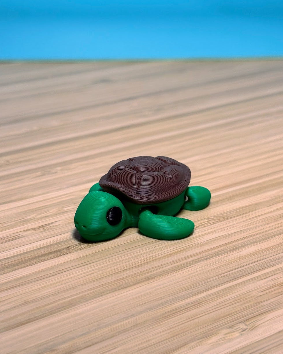 Green 3D printed Mini Flexi Turtle fidget toy with a brown shell on a wood desk