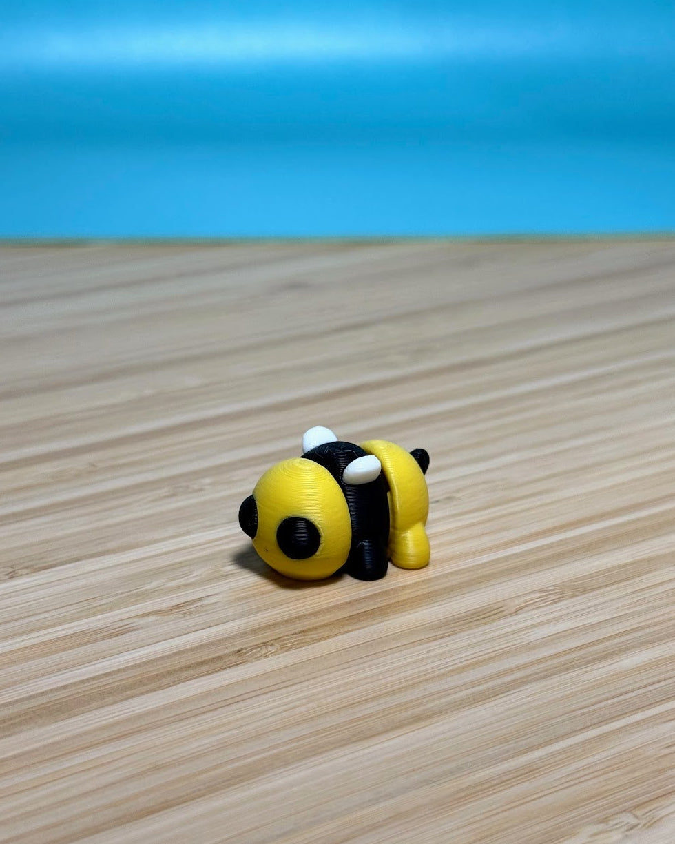 Yellow and black 3D printed Mini Flexi Bee fidget toy on a wood desk