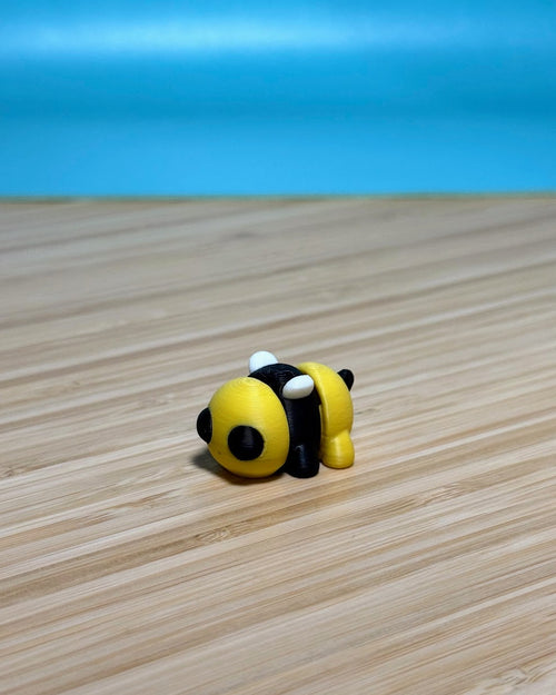 Yellow and black 3D printed Mini Flexi Bee fidget toy on a wood desk