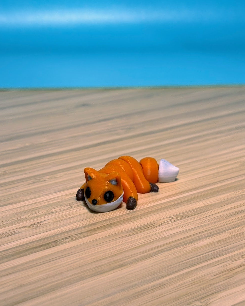 Orange 3D printed Mini Flexi Fox fidget toy on a wood desk