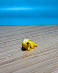 Yellow 3D printed Mini Flexi Triceratops fidget toy on a wood desk