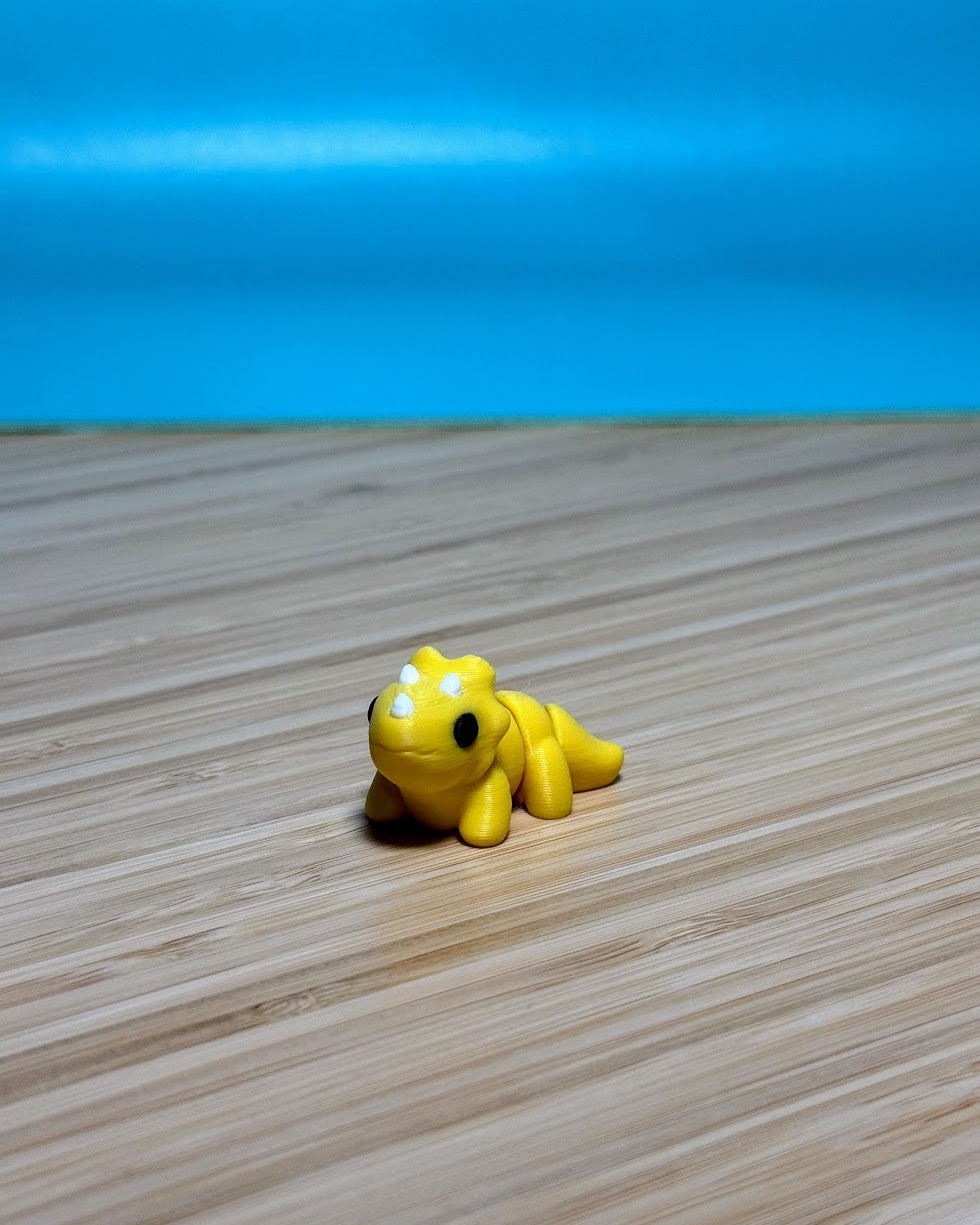 Yellow 3D printed Mini Flexi Triceratops fidget toy on a wood desk