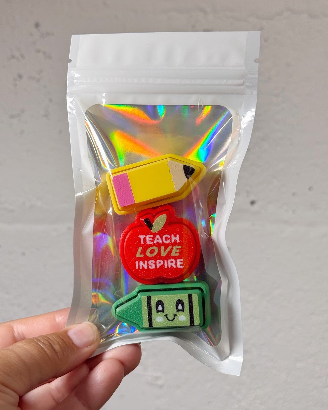 Teacher Clicky Pack in a holographic zip pouch: 3D printed pencil, red apple reading Teach Love Inspire, and green crayon clickies