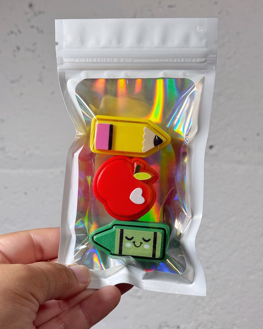 Teacher Clicky Pack pouch with a 3D printed pencil, plain red apple, and green crayon clicky, held in a hand