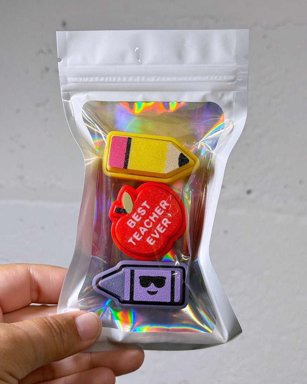Teacher Clicky Pack pouch with a pencil, a red apple reading Best Teacher Ever, and a purple crayon clicky, held in a hand