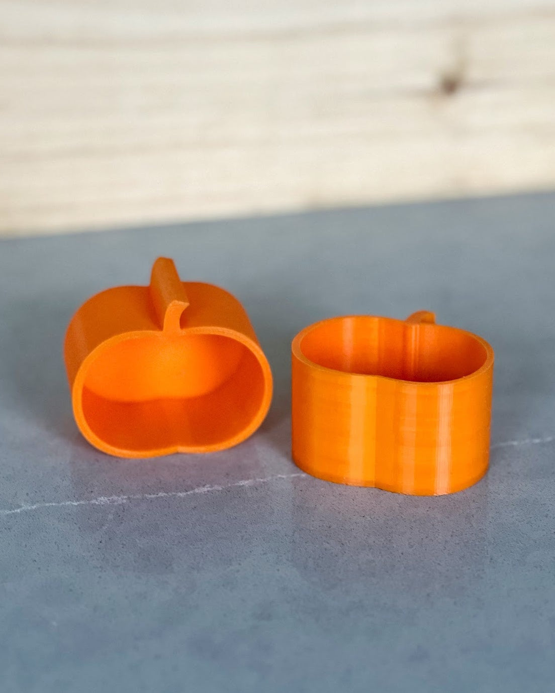 Two small orange 3D printed pumpkin plant pots, one lid open, on a gray surface