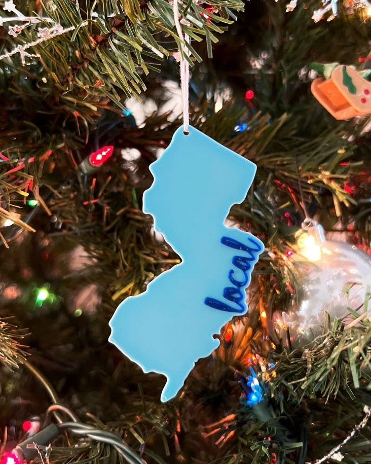 3D printed New Jersey shaped ornament with the word local in script, light blue, hanging on a lit Christmas tree