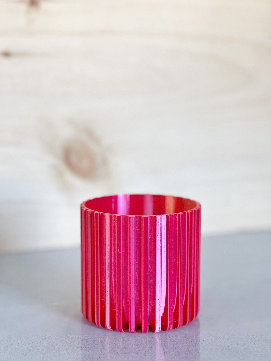 Empty iridescent pink and orange fluted 3D printed planter on a gray surface