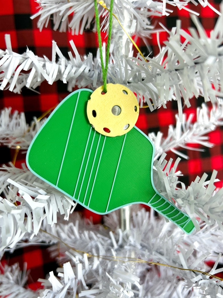 Green 3D printed pickleball paddle ornament with yellow ball hanging on a white Christmas tree