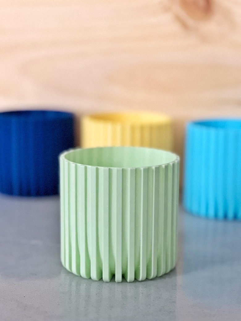 Mint green Modern Fluted Planter with dark blue, yellow and light blue planters behind it