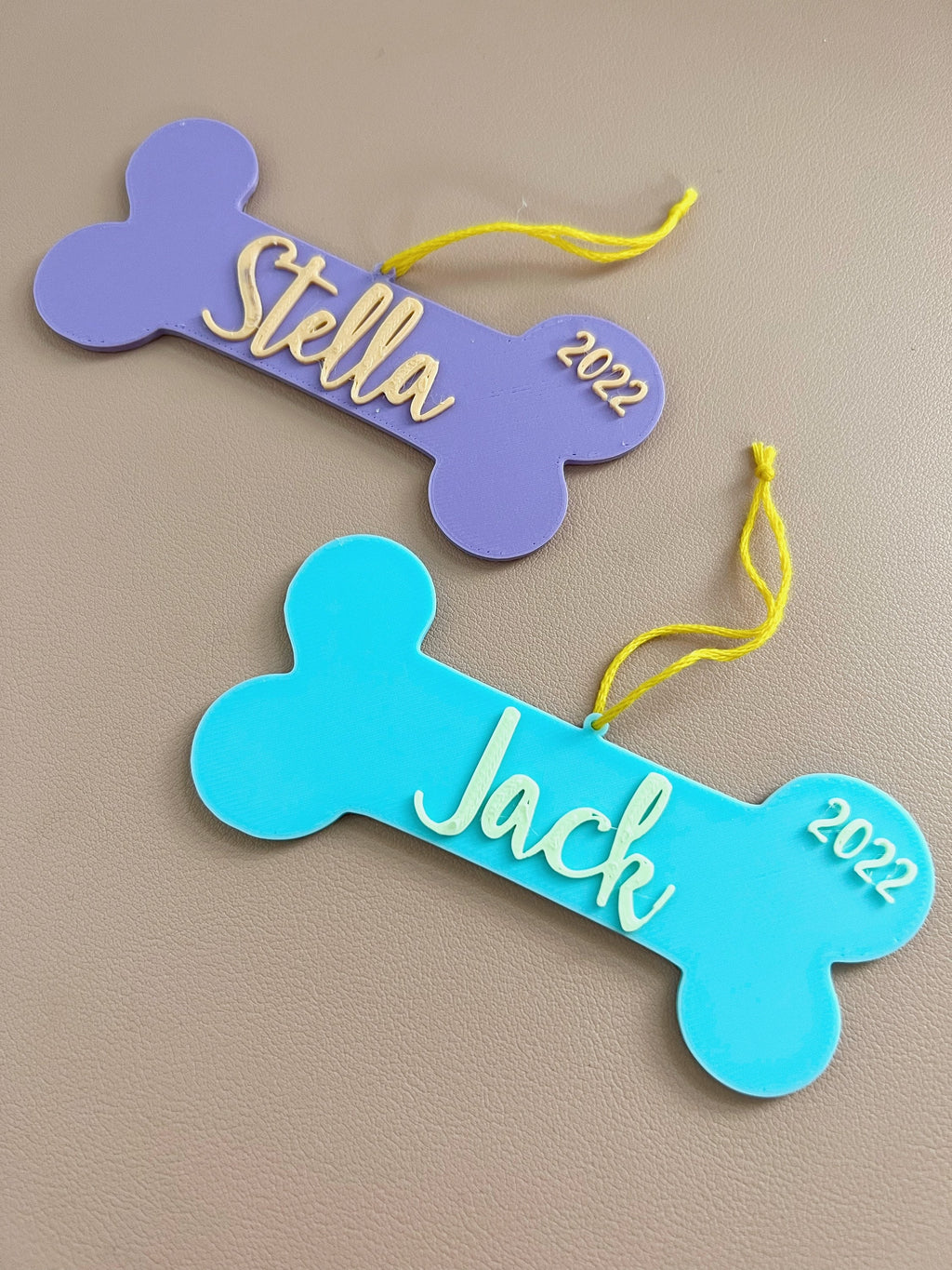 Stella and Jack personalized dog bone ornaments laid flat, showing both color options