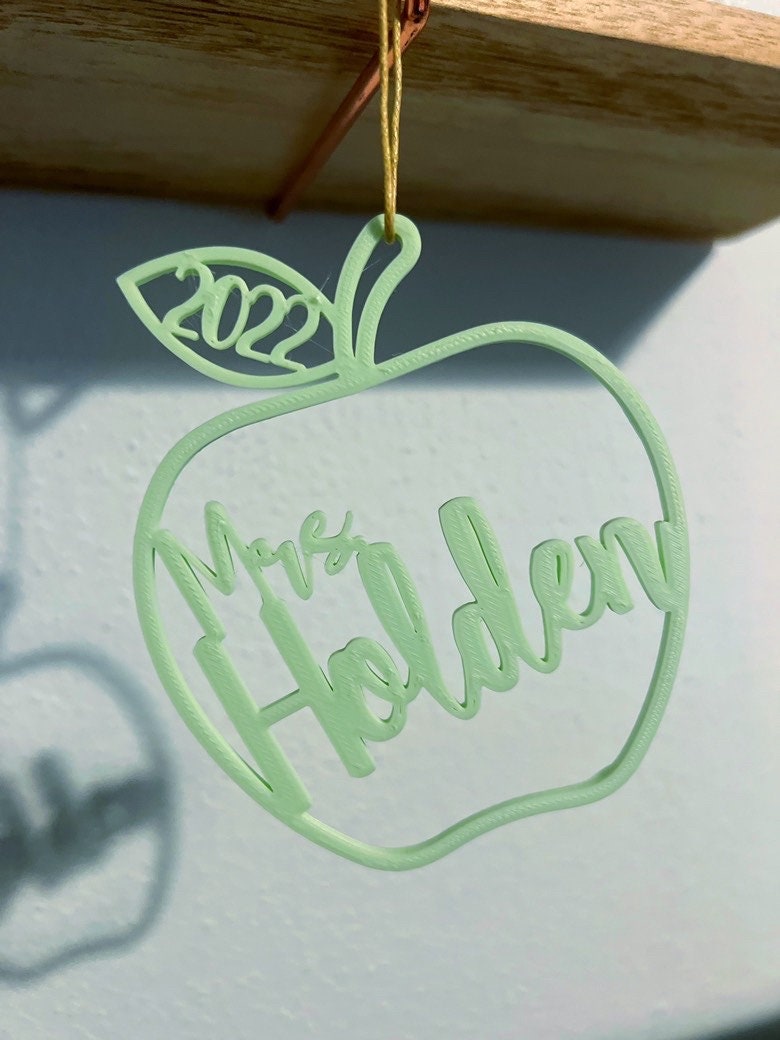 Mint green personalized apple ornament casting a shadow on a pink wall