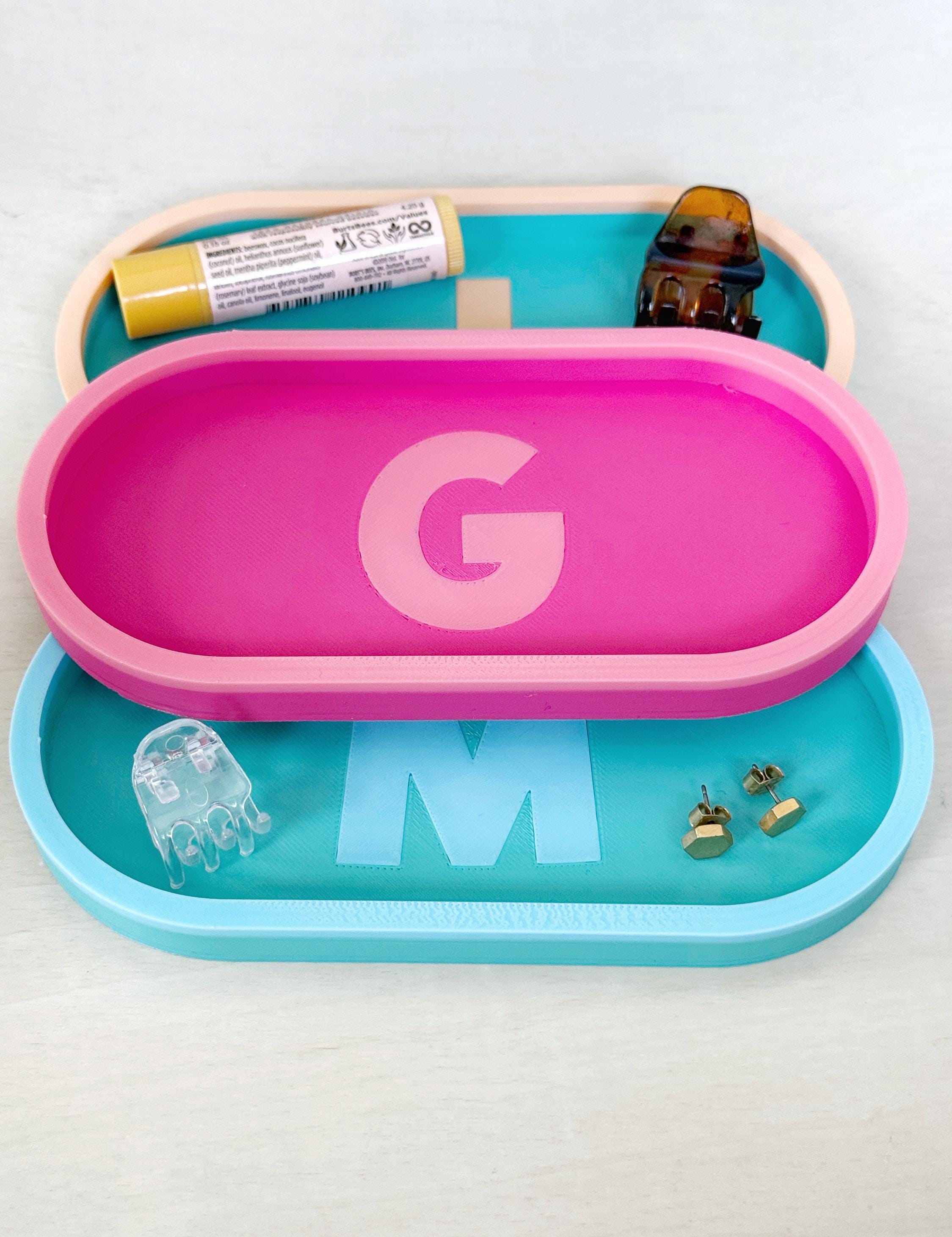 Pink and teal personalized initial catch-all trays with letters G and M holding small everyday items