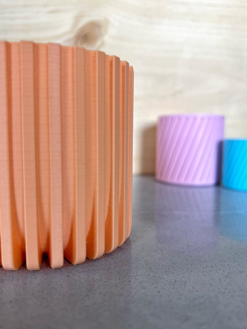 Peach 3D printed Modern Fluted Planter on a gray surface with lavender and blue planters behind it